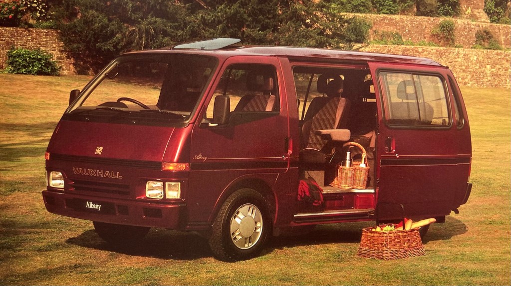 Front three-quarter of a red Vauxhall Albany with its sliding side door open, its front sunroof popped and a picnic awaiting being tucked into